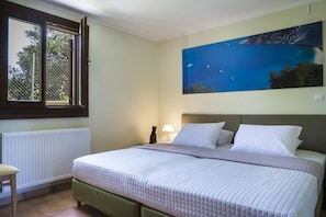 A bedroom with a bed, a nightstand, a lamp, a window with a view of the sea, and a painting on the wall.