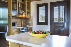 A kitchen with wooden cabinets, a stainless steel refrigerator, a microwave, and a stove. There is a bowl of vegetables on the counter.