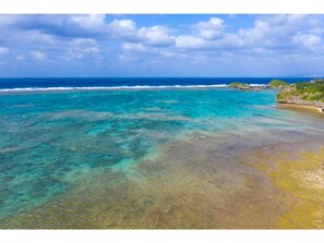 Paesaggio costiero con acque turchesi cristalline, spiaggia sabbiosa e affioramenti rocciosi.