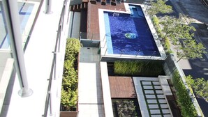 A modern building with a rooftop pool, surrounded by greenery and a paved walkway. - Strand Beachside 903 (Forster)