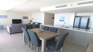 A modern kitchen with a dining area, grey furniture, and a flat-screen TV. - Strand Beachside 903 (Forster)