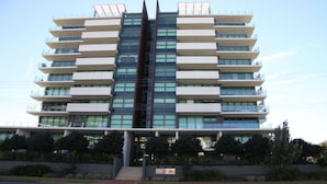 A modern multi-story building with a central glass facade, multiple balconies, and a sign indicating it is a hotel. - Strand Beachside 903 (Forster)