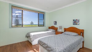 Ein Schlafzimmer mit zwei Einzelbetten, einem Fenster mit Blick auf Bäume und eine entfernte Landschaft, sowie zwei an der Wand befestigte Kunstwerke.