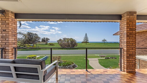A balcony with a view of a road and greenery, a bench, and a tiled floor.