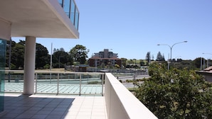 A balcony with a view of a building, a fence, and trees. - The Reef 103 - Lakeside! (Forster)