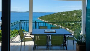 A balcony with a table and chairs overlooking a coastal view.