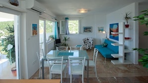 A dining area with a glass table and white chairs, a blue sofa, and a white wall with a painting.