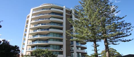 A multi-story hotel with balconies on each floor, surrounded by trees.