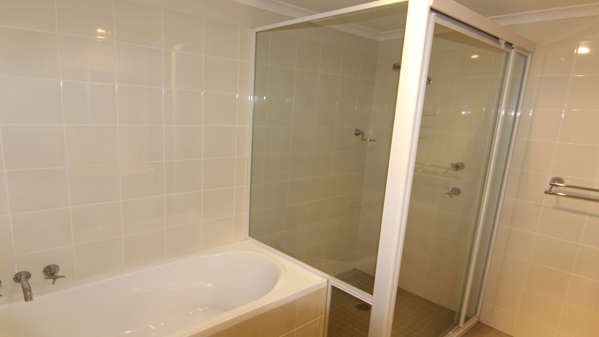 Ein Badezimmer mit einer Glaskabine zur Dusche, einer weißen Badewanne und einer gefliesten Wand.
