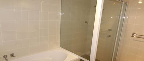 Ein Badezimmer mit einer Glaskabine zur Dusche, einer weißen Badewanne und einer gefliesten Wand.