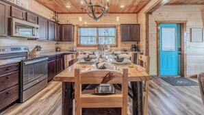 L’intérieur d’un chalet en bois comprend une cuisine avec des meubles sombres, un îlot central doté de chaises, un lustre et une porte bleue.