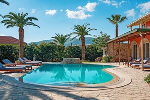 A pool area with lounge chairs, palm trees, and a stone building with arches. - Amor Beach Villa 3 Bedrooms with huge pool, BBQ, near the beach. (Zakynthos)