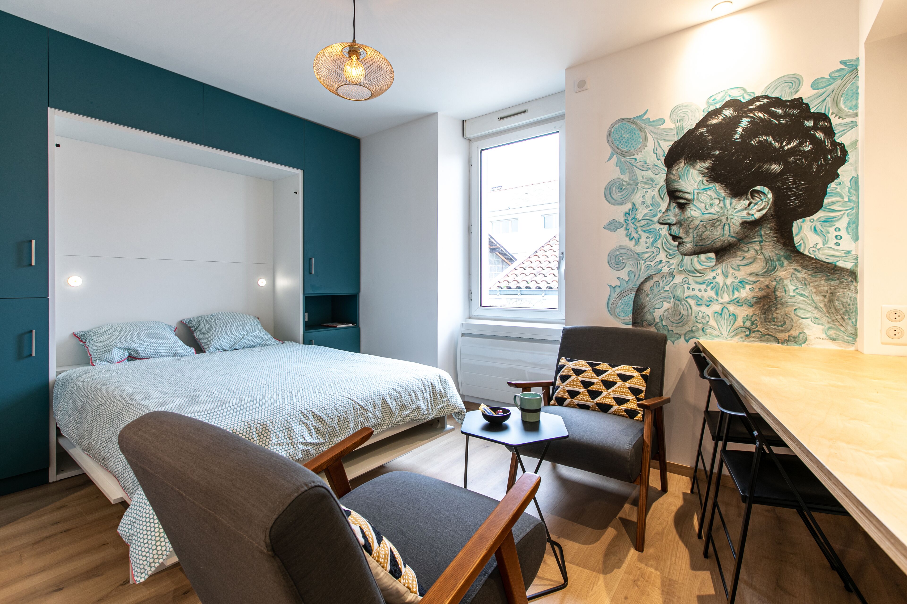 Ein modernes Schlafzimmer mit Bett, Schreibtisch und Stuhl. Ein Fenster bietet Blick auf die Stadt.
