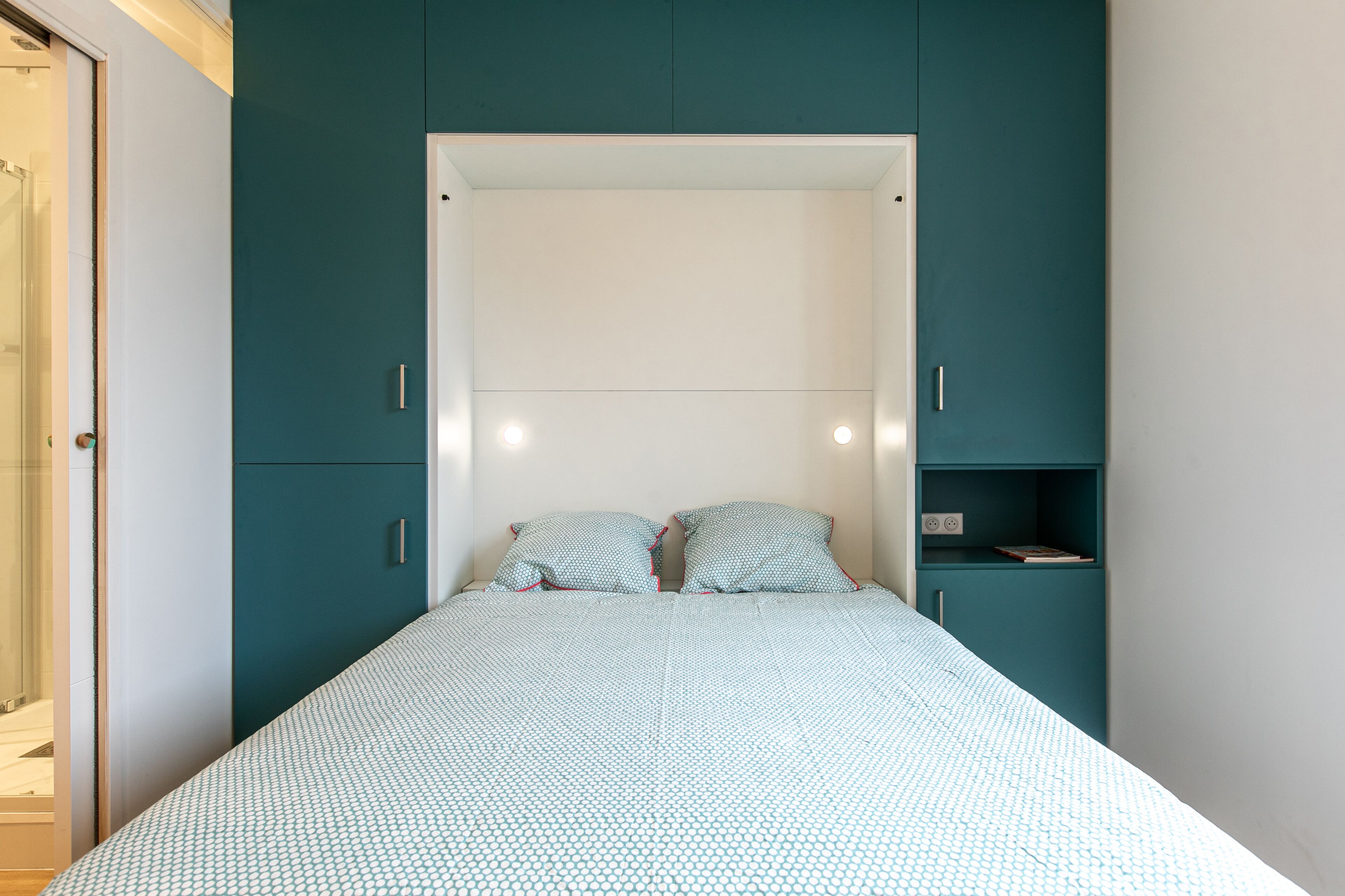 Una camera da letto con un letto, mobili color acquamarina e una testiera bianca.