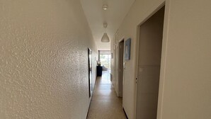 En lång, smal hall med vita väggar och ett fläckigt golv, som leder fram till en dörr i slutet.