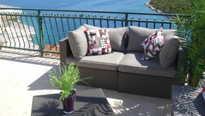 Ein Balkon mit einer Rattan-Couch, zwei gemusterten Kissen und einem Blumentopf.