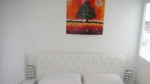 Ein Schlafzimmer mit einem weißen Bett, zwei Nachttischen mit Dekoration und einem Bild an der Wand.