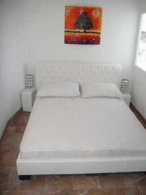 A bedroom with a white bed, two bedside tables with decorative items, and a painting on the wall. - Two Bedroom Apartment with Balcony (Vinišće)