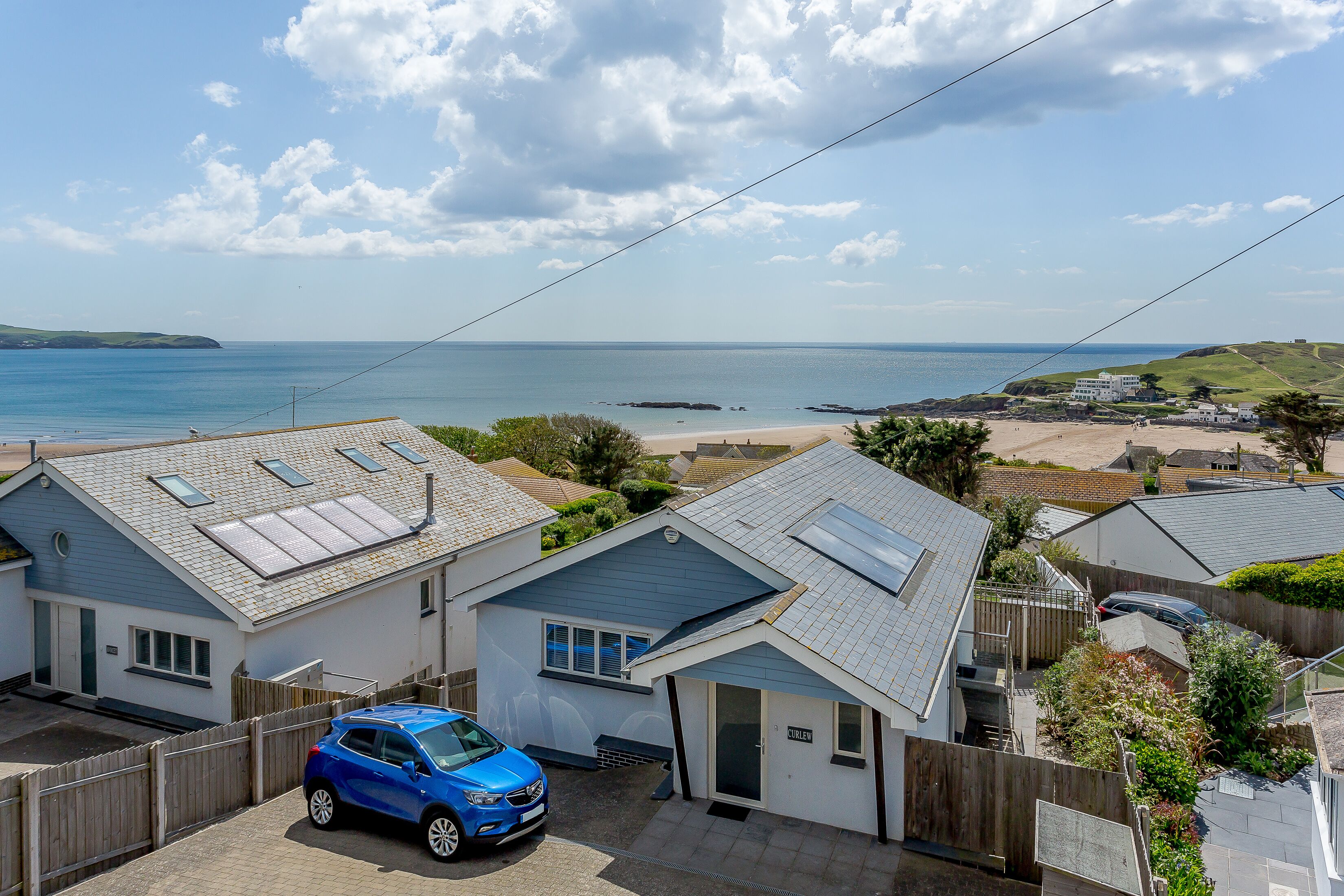 Un quartier résidentiel avec des maisons, une voiture bleue et une vue sur la mer.