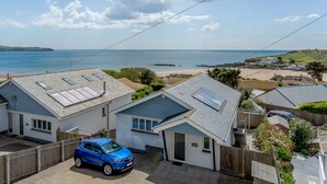 A residential area with houses, a blue car, and a view of the sea. - Luxury property Sleeps 8 - Sea views & hot tub - 200m from beach! (Bigbury-on-Sea)