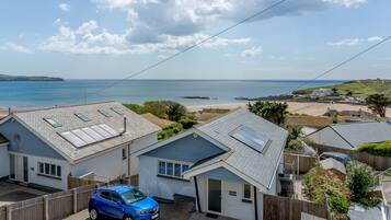 Un quartier résidentiel avec des maisons, une voiture bleue et une vue sur la mer.