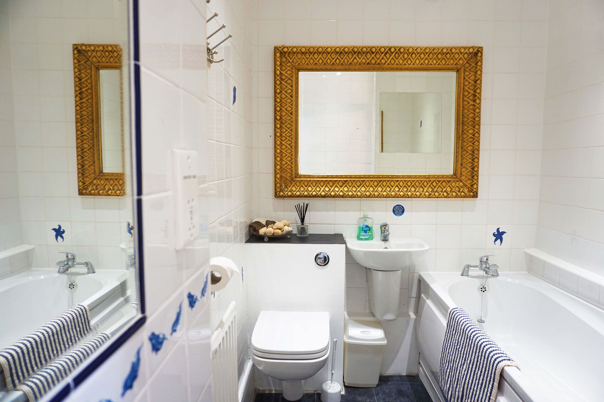 Un bagno compatto con vasca, lavabo e WC. Le pareti sono rivestite da piastrelle decorative e c'è uno specchio con cornice ornata.