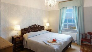 A bedroom with a large bed, two bedside lamps, a chandelier, a window with curtains, and a view of the sea. - 1h from central London and 30min from Dover, opposite stairs to sandy beach (Broadstairs)