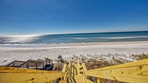 Een strand met een houten vogelbeschutting langs een zandstrand, een heldere blauwe lucht en de oceaan op de achtergrond.