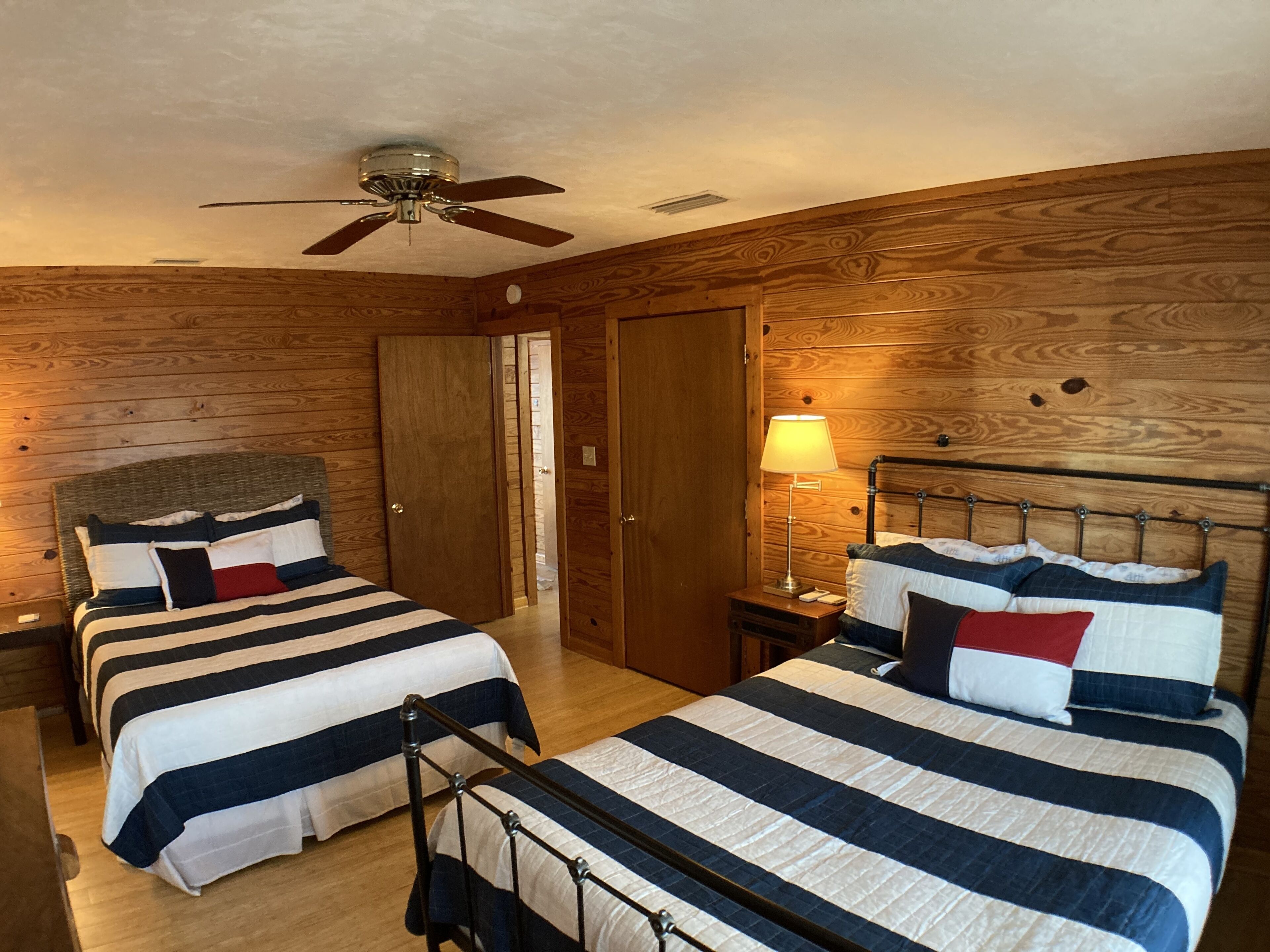 Ein Schlafzimmer mit zwei Betten, Holzwänden, einem Deckenventilator und einem Nachttisch mit Lampe.