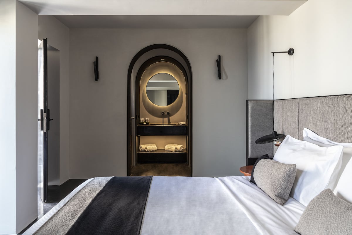A modern hotel room with a large bed, a built-in vanity with a mirror, and a bedside table with a lamp.