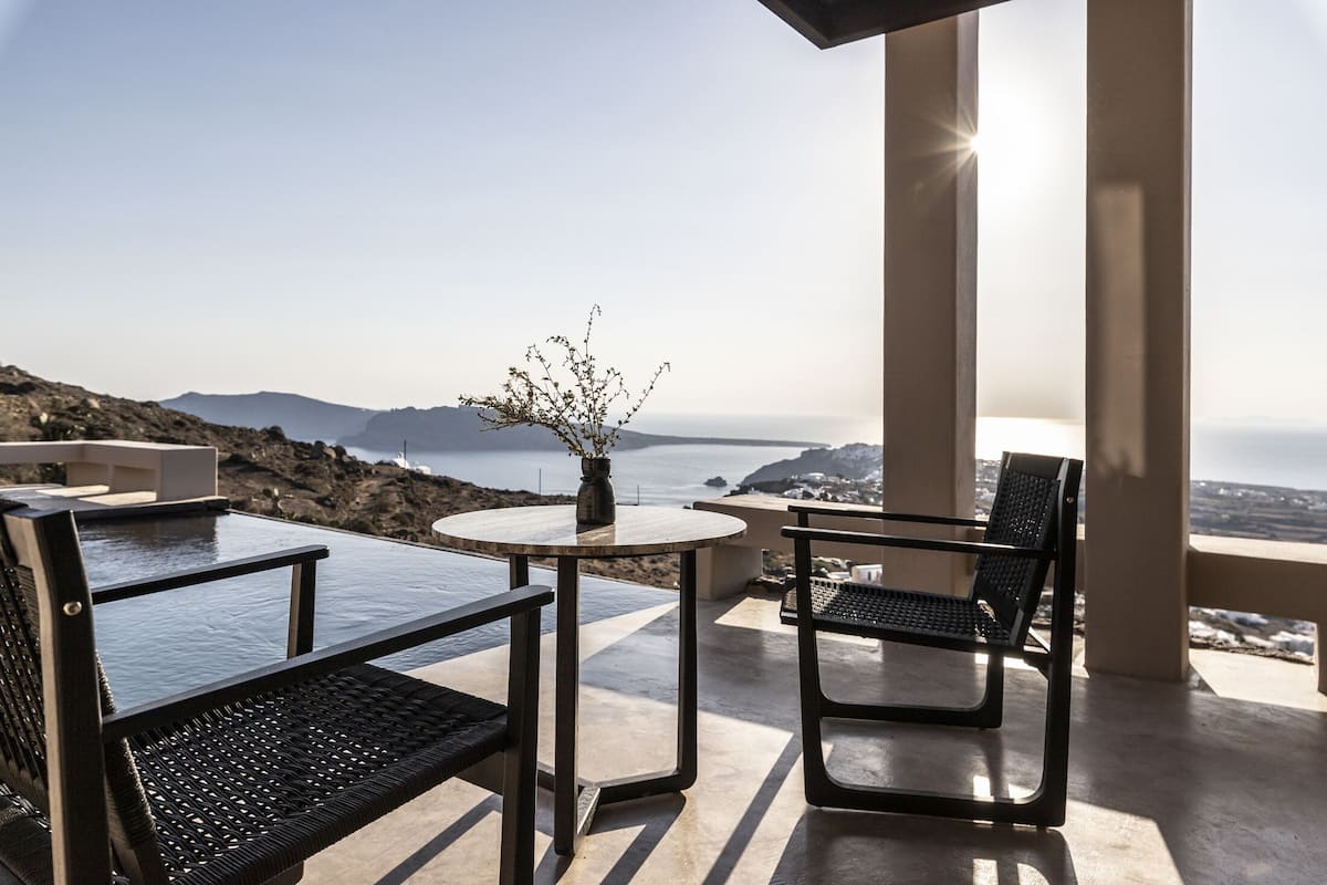 A terrace with a table and chairs, overlooking a coastal view with mountains in the distance.