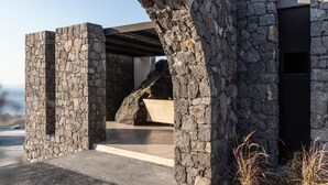 A stone structure with a modern design, featuring a large rock formation and a concrete bench. - Nimbus Santorini (Santorini)