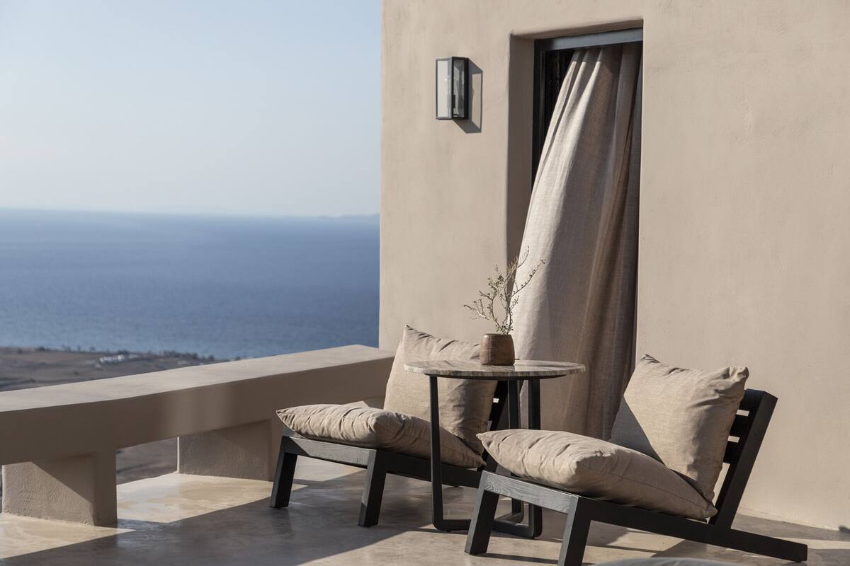 A balcony with a view of the sea, featuring two chairs and a small table with a vase.