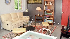 Un salon avec un canapé beige, une table basse en verre, une bibliothèque et une porte rouge.