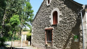 Un bâtiment en pierre doté d’une petite fenêtre en arc de cercle et d’une porte, entouré d’arbres et d’une clôture en bois.