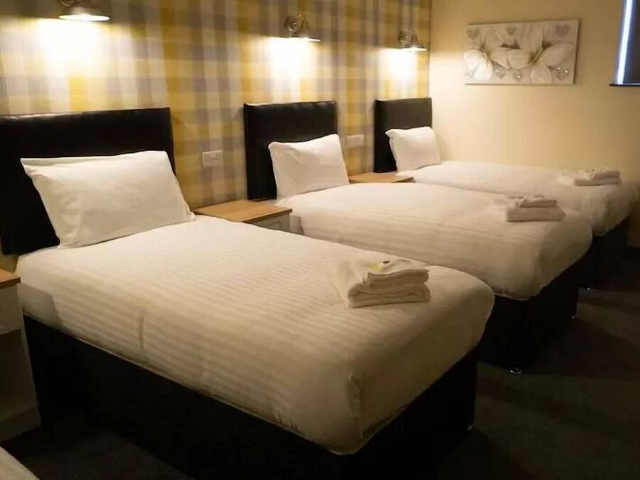 Habitación de hotel con tres camas individuales, cada una con cabecera y mesitas de noche.
