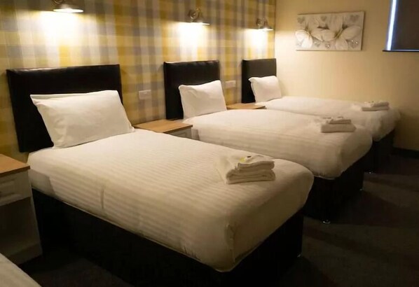 Une chambre d’hôtel avec trois lits simples, chacun doté d’une tête de lit et de tables de chevet.