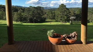 A wooden deck with two terracotta pots on a sunny day overlooking a green field and trees. - Cottage Sleeps 13 - Stunning Views! (Berambing)