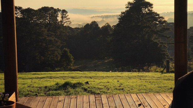 A view from a covered porch overlooking a grassy field with trees and a distant mountain range. - Cottage Sleeps 13 - Stunning Views! (Berambing)