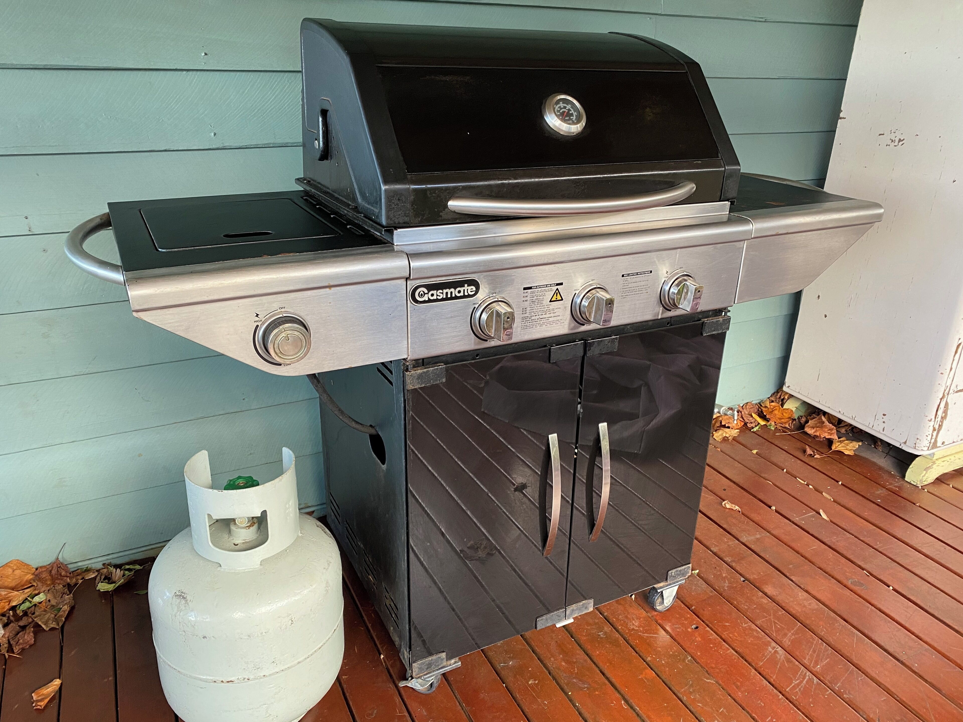 A gas-powered grill with a side burner, a storage cabinet, and a propane tank.
