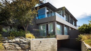 Een modern, twee verdiepingen hoog huis met grote ramen, een gevel van natuursteen en een aangelegde tuin met rotsen en planten.