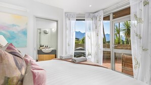 Een slaapkamer met een groot bed, een badkamer met een wastafel en spiegel, en een balkon met uitzicht op bergen.