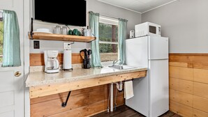 A compact kitchen with a wooden countertop, a white refrigerator, a microwave, and a window with curtains.
