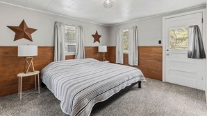A bedroom with a bed, two star-shaped wall decorations, a lamp on a side table, and a door with a window view.