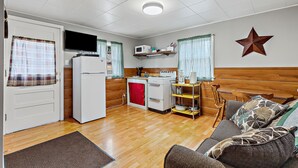 A compact kitchen with a microwave, stove, and refrigerator. There is a wooden bench and a sofa with patterned cushions.
