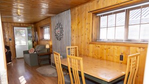 A wooden interior with a dining table and chairs, a sofa, and a decorative wall piece. - The Peggy! (Creede)