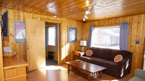 A wooden cabin interior with a sofa, a table, and a lamp. - The Peggy! (Creede)