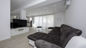 Uma sala de estar moderna com um amplo sofá modular, uma TV de tela plana e uma mesa de centro de vidro.