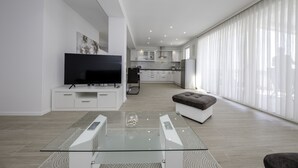 Uma sala de estar moderna com uma mesa de centro de vidro, uma televisão de tela plana e uma área de estar confortável.