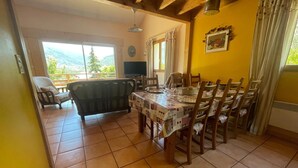 A dining area with a table set for four, wooden chairs, a sofa, and a television in the background.